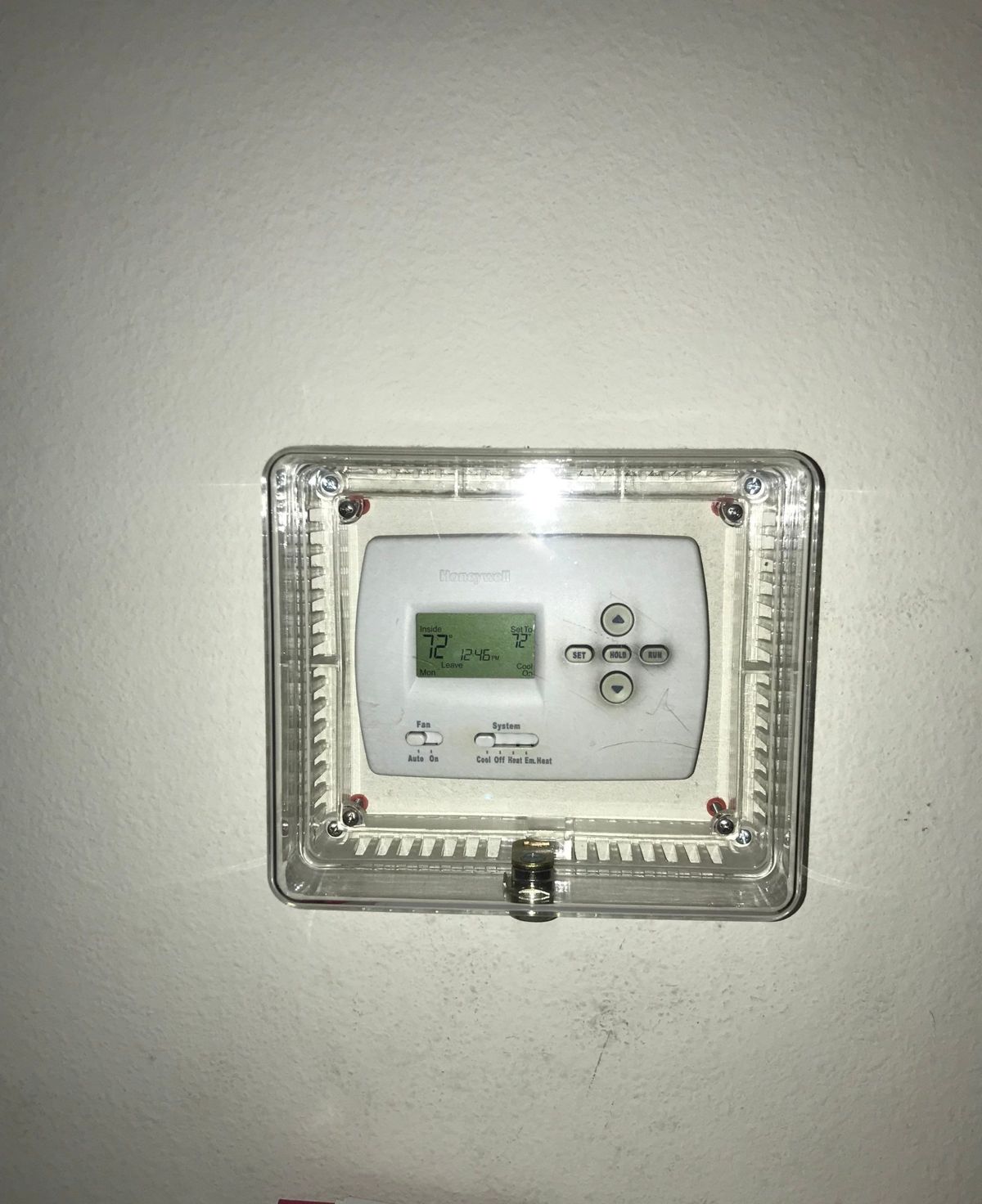 Old thermostat under a locking cover before replacement