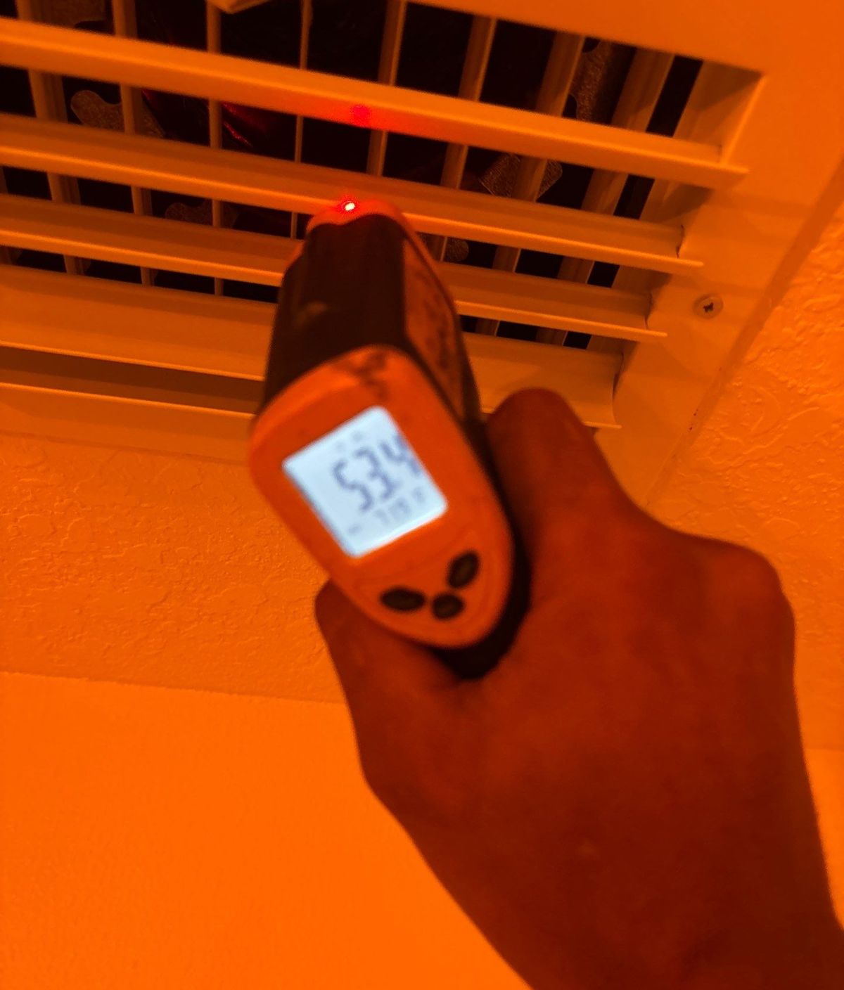 Technician checking supply air temperature at a grille after duct replacement