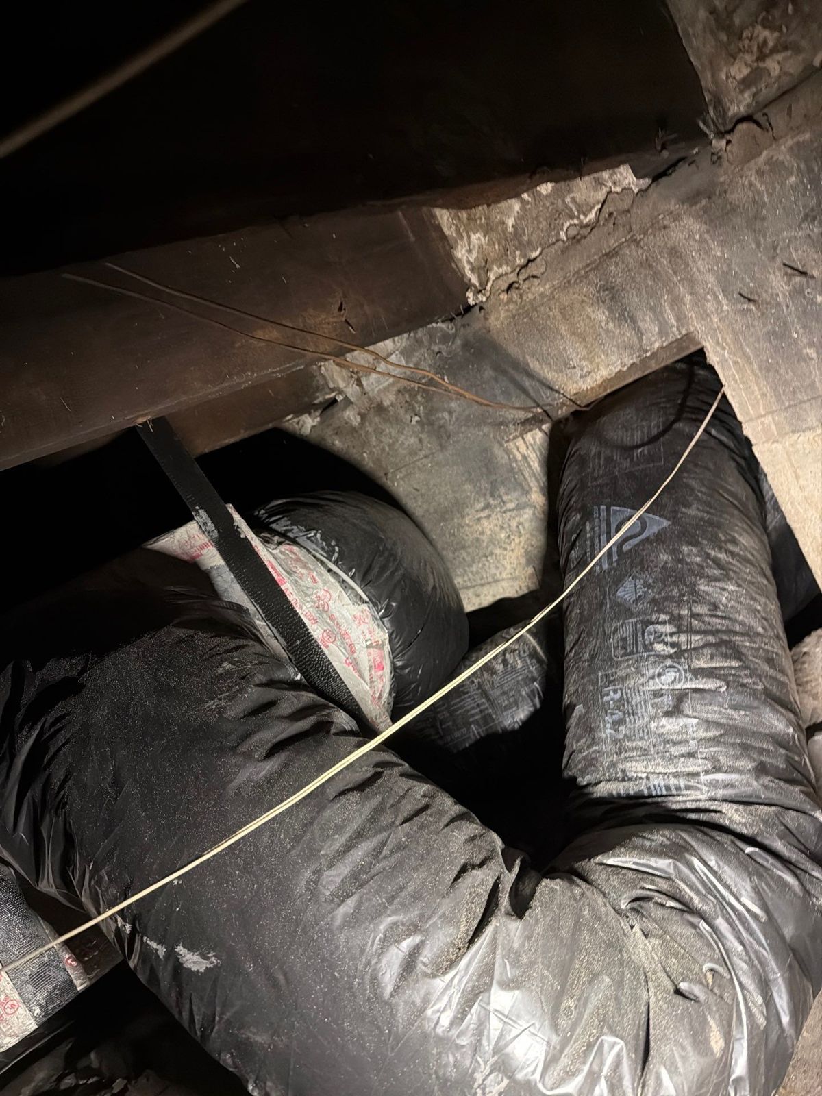 Old flex duct runs crossing between floor joists in a crawlspace