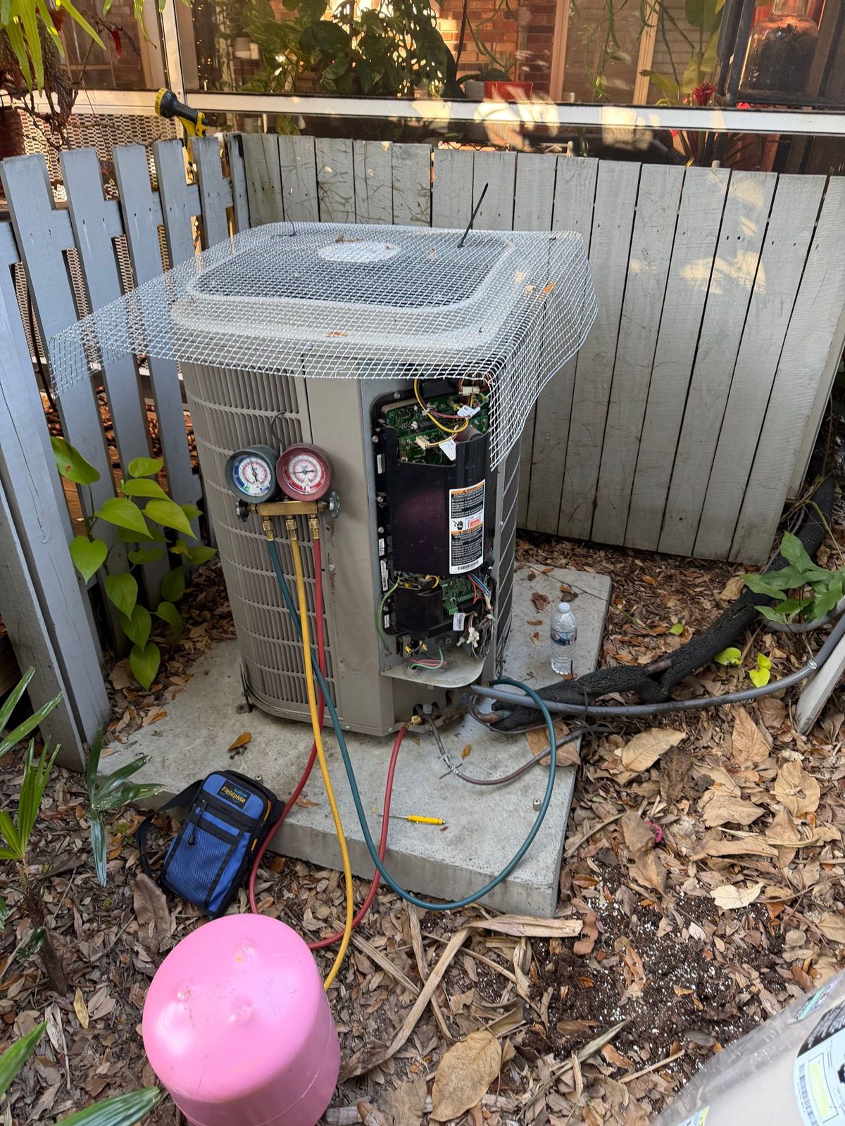 Old outdoor unit beside a fence in South Tampa before heat pump replacement